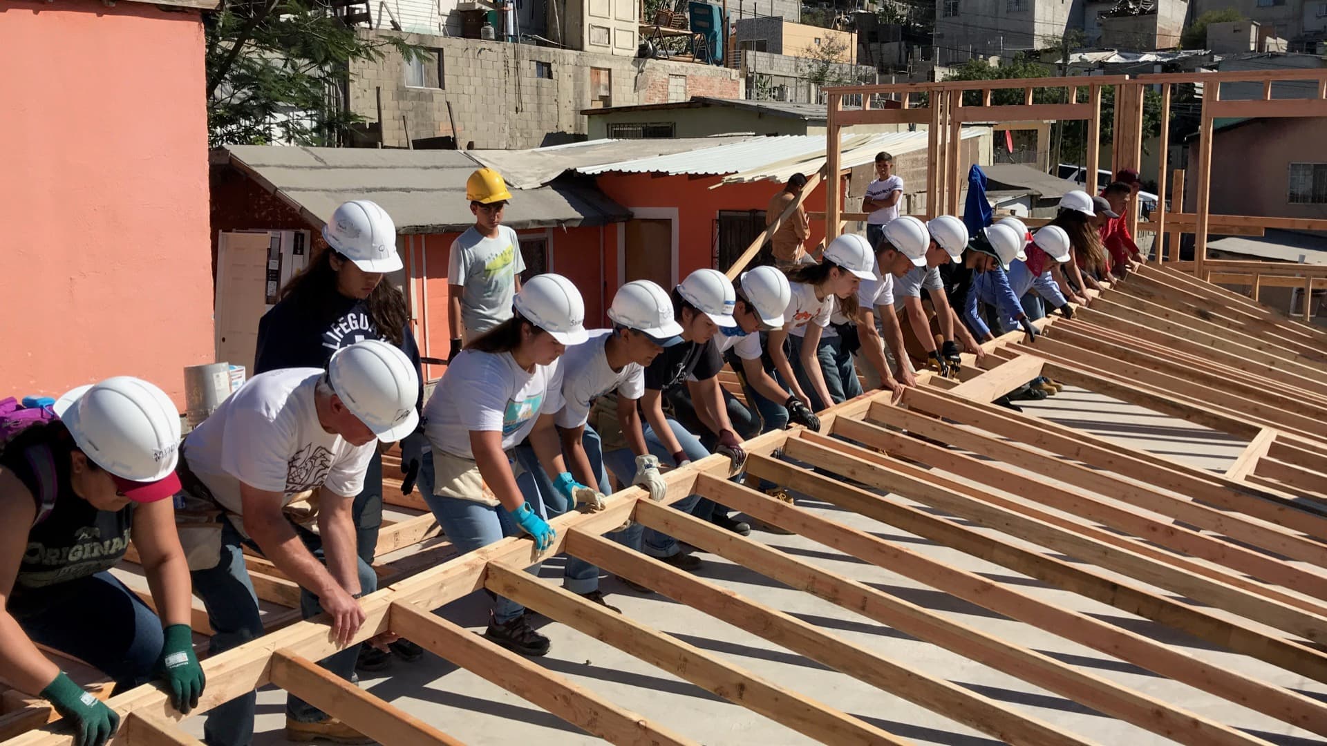 Volunteers in hard hats raising a wooden roof frame together